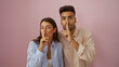 © Krakenimages.com - Couple making shushing gesture with fingers on lips while standing against a pink background, expressing secrecy or quietness