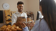 © Krakenimages.com - Man serving coffee to woman in bakery with shelves of bread in the background and a clock on the wall