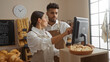 © Krakenimages.com - Man and woman working together in a bakery shop, discussing orders at a computer, surrounded by shelves with bread and pastries