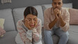 © Krakenimages.com - Couple sitting in a living room with a woman looking stressed and man appearing thoughtful, suggesting relationship issues in a home interior setting.