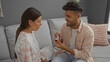 © Krakenimages.com - Man proposing to woman with ring box in living room, the couple seated on sofa has a serious emotional moment, indicating a relationship milestone, indoors with cozy home decor.