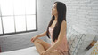 © Krakenimages.com - Young chinese woman sitting on bed in bright bedroom with white brick walls, enjoying morning light from window indoors at home