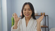 © Krakenimages.com - Woman waving happily in a spa room, wearing a white robe with a relaxing spa interior, emphasizing her joy and wellness