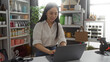 © Krakenimages.com - Asian woman working on a laptop in a home decor store filled with various products, showcasing a modern and stylish interior setting.