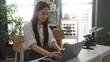 © Krakenimages.com - Young chinese woman working on a laptop in a home decor shop with indoor greenery and shelves full of decorative items in china.
