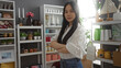 © Krakenimages.com - Young, attractive, chinese woman with crossed arms stands confidently in a well-decorated home decor shop, surrounded by various interior design items and plants