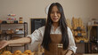 © Krakenimages.com - Young woman with long hair standing in a bakery shop in china, smiling and wearing an apron in an indoor setting with bread and pastries on display.