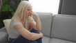 © Krakenimages.com - Woman with albinism sitting thoughtfully on a gray sofa in a bright living room, embodying reflection and tranquility in a cozy home setting.