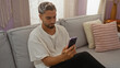 © Krakenimages.com - Young man with beard using smartphone in cozy living room