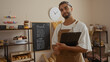© Krakenimages.com - Man standing in a bakery with a clipboard, surrounded by pastries and bread, with shelves and menu chalkboard in the background