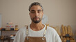 © Krakenimages.com - Handsome young man with a beard standing in a bakery wearing an apron, showcasing assorted baked goods on shelves in the background