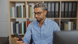 © Krakenimages.com - Young arab man with beard and glasses in office reading smartphone indoors surrounded by books and documents
