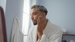 © Krakenimages.com - Young man with beard in white robe applying skincare product at wellness spa indoors