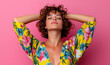© hocine - Young woman with curly hair poses gracefully against a vibrant pink background wearing a colorful floral dress, radiating confidence and joy in summer fashion