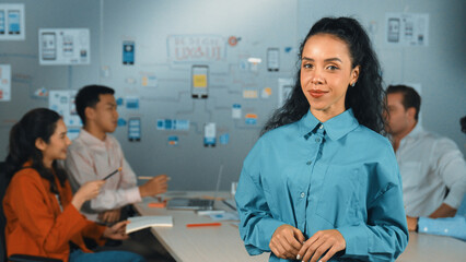 Wall Mural - Hispanic professional businesswoman standing with arm folded at creative business meeting. Beautiful confident leader crossing arm while diverse business people discussion about plan. Manipulator.