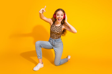 Wall Mural - Joyful young woman wearing leopard print top, listening to music with headphones against yellow background