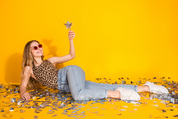 Wall Mural - Stylish young woman in leopard print top celebrating with confetti on yellow background, bringing vibrant energy to fashion lifestyle