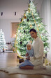 © saulich84 - A mother in a white sweater sits with her daughter for 1 year on the floor by the Christmas tree in an apartment on New Year's Eve