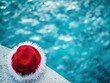 © Philipp - Festive hat by the pool with shimmering water, suggesting an unusual vacation scene. Ideal for holiday promotions and seasonal travel campaigns.