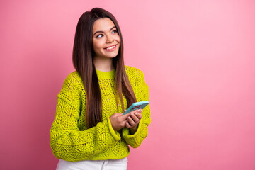 Wall Mural - Smiling young woman in vibrant knitwear holding smartphone against pink background, showcasing youth, style, and casual charm