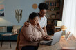 © Seventyfour - Accommodating African American female social worker assisting elderly woman with laptop use paying bills online at wooden desk in cozy apartment