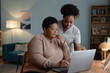 © Seventyfour - Supportive African American female social worker assisting elderly woman with laptop use explaining how to pay bills online while sitting at desk in cozy living room, copy space