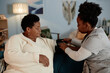 © Seventyfour - Female nurse wrapping cuff of automatic tonometer on elderly Black womans arm measuring blood pressure during health checkup visit at home