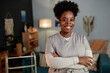 © Seventyfour - Medium portrait of African American female social worker beaming with smile wearing scrubs posing with arms crossed during house visit to patient, copy space
