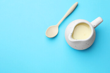 Wall Mural - Tasty condensed milk in jug and spoon on light blue background, top view. Space for text