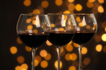 Wall Mural - Tasty red wine in glasses against dark background with blurred lights, closeup. Bokeh effect