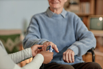 Cropped shot of elderly man putting finger on oximeter sensor checking up oxygen saturation in blood during social worker visit at home, copy space