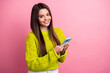 © deagreez - Stylish young woman in trendy knitwear smiling while holding smartphone against a pink background