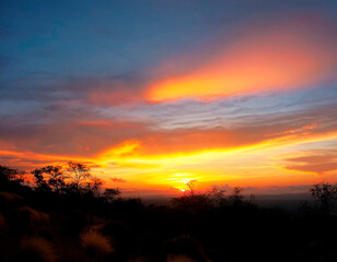 Fototapete - Bello atardecer con cielo naranja, amarillo, rojo y azul, sobre la montaña.
