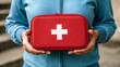 © Walid Forhad - Preparedness in Hand: A close-up of a woman's hands holding a bright red first aid kit, symbolizing preparedness and the importance of being ready for any emergency.