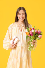 Canvas Print - Beautiful young pregnant woman with bouquet of tulips and gift box on yellow background. International Women's Day