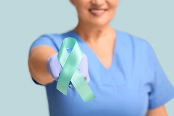 Wall Mural - Mature female doctor with teal ribbon on blue background, closeup. Cervical Health Awareness Month