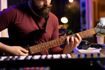 Leinwandbilder - Musical artist playing acoustic guitar and recording a new song in home studio, using modern acoustical engineering tools. Composer creating new audio sounds on instrument, post production.
