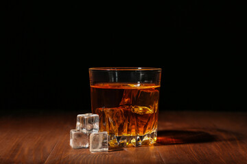 Wall Mural - Glass of rum with ice cubes on wooden table against black background