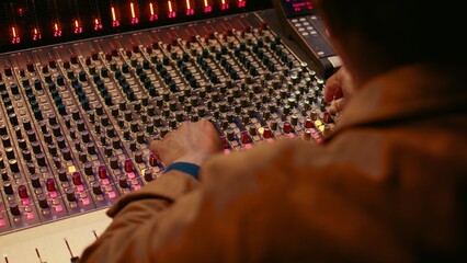 Fototapete - Audio technician producing new music at mixing console in control room, twisting knobs, pressing sliders and switchers. Producer working on processing and editing sounds quality. Camera B.