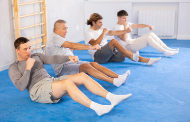 Wall Mural - Group of men of different ages train abdominal muscles and do punches at the same time during karate or judo training