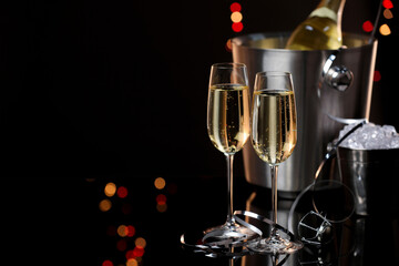 Champagne in glasses, bottle and ice buckets on mirror surface against black background with blurred lights, space for text