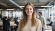 © Jaroon - Confident Young Professional: A smiling young woman with long brown hair stands confidently in a modern office environment, her radiant smile reflecting success and optimism.