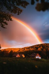 Wall Mural - Rainbow arc over houses on hill, with trees framing view; inspiring travel image