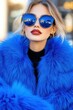 © Natalia - Stylish woman in a fluffy blue faux fur coat enjoys coffee outdoors at a trendy café with a moody ambiance