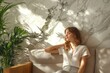 © Isuru - Young woman rests on a beige couch against a marble wall, bathed in sunlight and surrounded by plants.