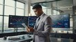 © ittipol - Strategic Analysis:  A focused businessman in a sharp suit stands in front of a bank of monitors displaying financial data, meticulously reviewing information on a digital tablet.
