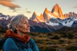 © Isuru - A serene older woman admires the majestic, sunlit Fitz Roy massif in Patagonia, a breathtaking landscape.