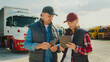 © VAKSMANV - Caucasian man and woman standing at truck pit stop. Discussing something while looking at information on tablet device. Having issues about order information or delivery confirmation from customer.