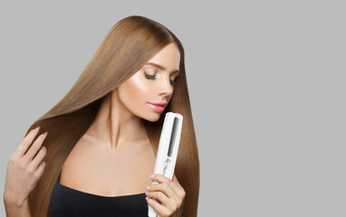 Wall Mural - Glad smiling woman with long straight healthy hairstyle using straightening iron on white background. Beauty, hair care, hair treatment and cosmetic concept