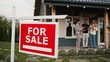 © VAKSMANV - Camera focus on sign hanging in front of entrance to house. In blurred background people discussing with real estate agent possible price for property. Family looking for new home.